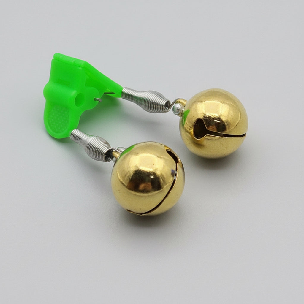Gold bells with a green plastic clip on a reflective black surface